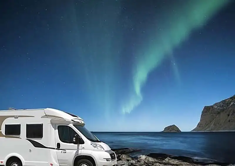 Northern Lights display next to a campervan in Iceland.